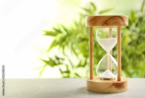 Hourglass with flowing sand on table against blurred background. Time management