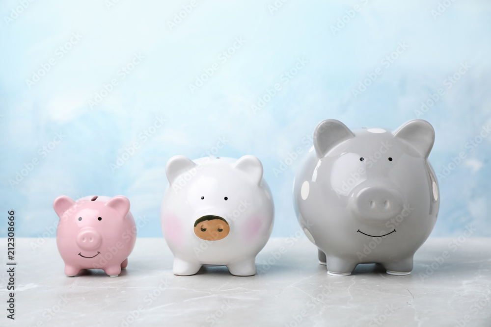 Three cute piggy banks on table against color background