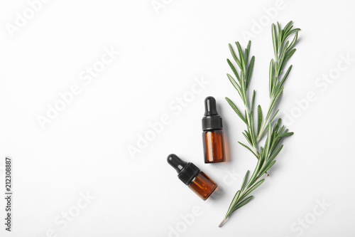 Bottles of rosemary oil and fresh twigs on white background  top view