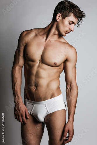 Male model with perfect body in white underwear posing over grey background. Close-up. Studio shot.