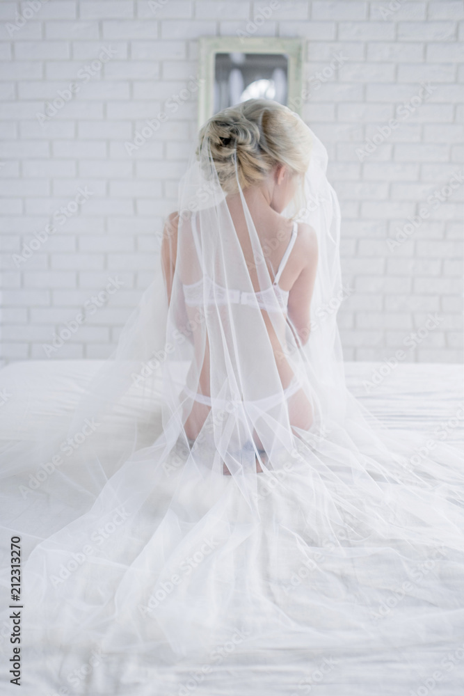 Beautiful bride in white lingerie sits on the bed hidden under the veil Beautiful bride in white lingerie sits on the bed hidden under the veil
