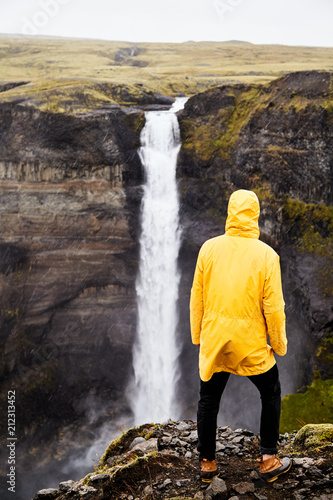 Waterfall Haifoss in Iceland. A young guy stands on a cliff and looks at the waterfall. 