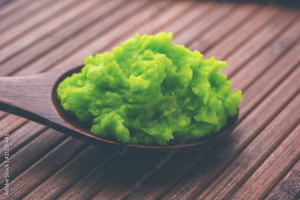 Green wasabi sauce or paste in bowl, with chopsticks or spoon over plain colourful background. selective focus