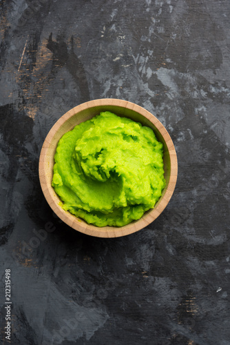 Fotografia Green wasabi sauce or paste in bowl, with chopsticks or spoon over plain colourful background