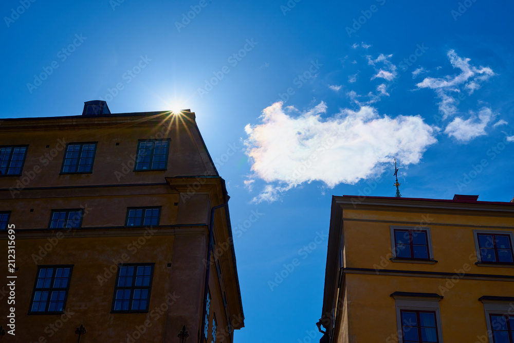 Sunrays behind the houses with blue sky and clouds on a background. Sunrays behind the houses with blue sky and clouds on a background.