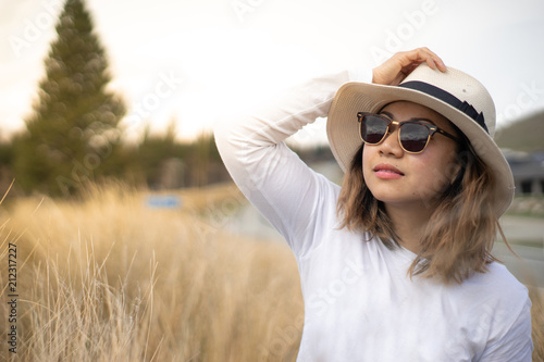close up head shot of an Asian traveller in white long sleeve t shirt, wears sunglasses and white hat in grass field 