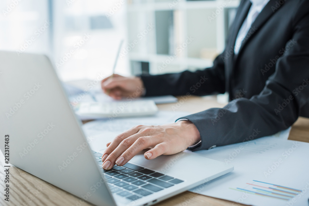 cropped image of financier using laptop at table in office cropped image of financier using laptop at table in office