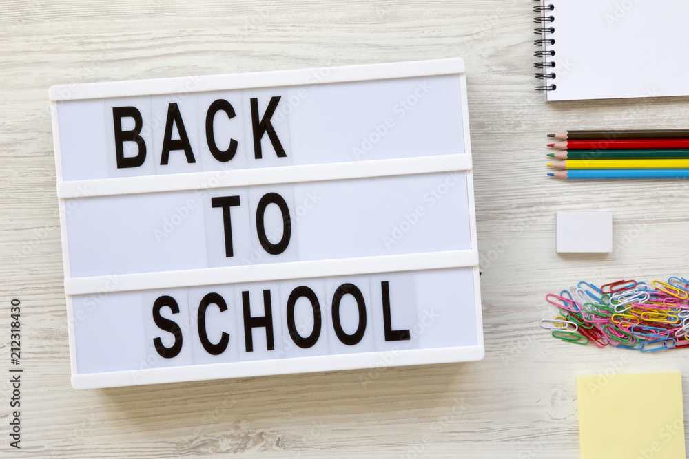 'Back to school' word on lightbox, accessories for study over white wooden background, from above. Top view.