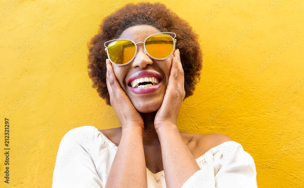 Φωτογραφία Fashion african woman smiling and wearing sunglasses with yellow ochre backgroun