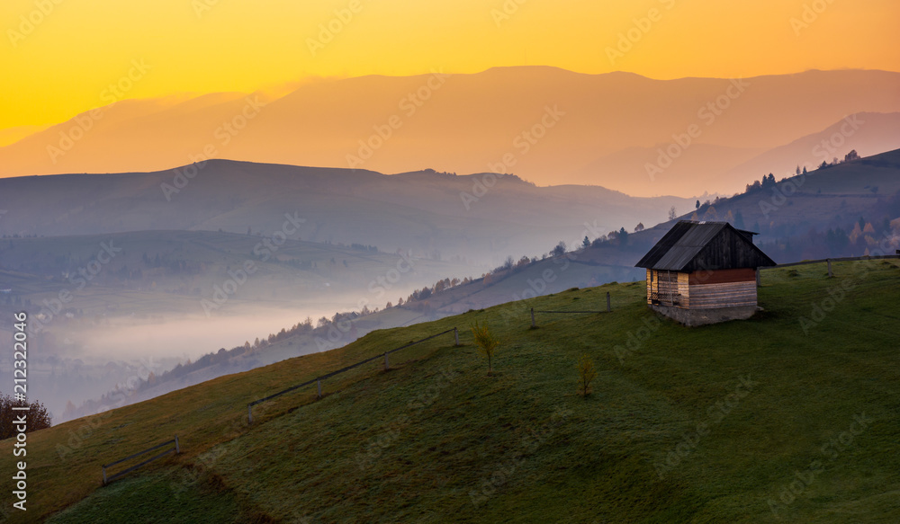 woodshed on a hillside at sunrise. beautiful countryside scenery of mountainous area. yellow sky over the purple mountains. fog down the valley of Synevir village, TransCarpathia, Ukraine