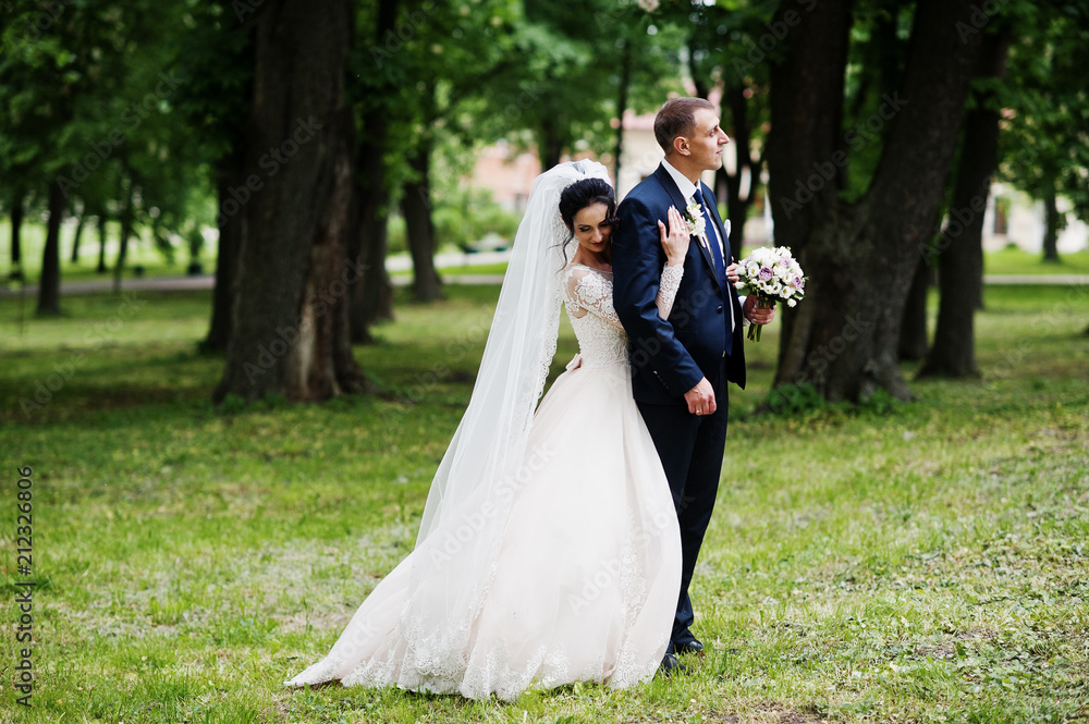 Gorgeous and happy newly married couple standing in green park on their wedding day.