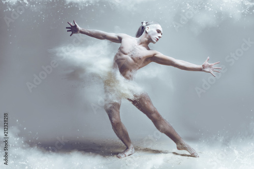 Dancing in flour concept. Naked muscle man dancer in dust / fog. Guy wearing white shorts making dance element stretching his arms in flour cloud on isolated background