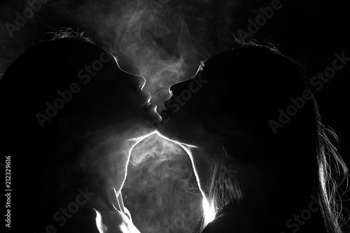 Canvas Print Silhouette of two sexy woman kissing holding in darkness through light and smoke
