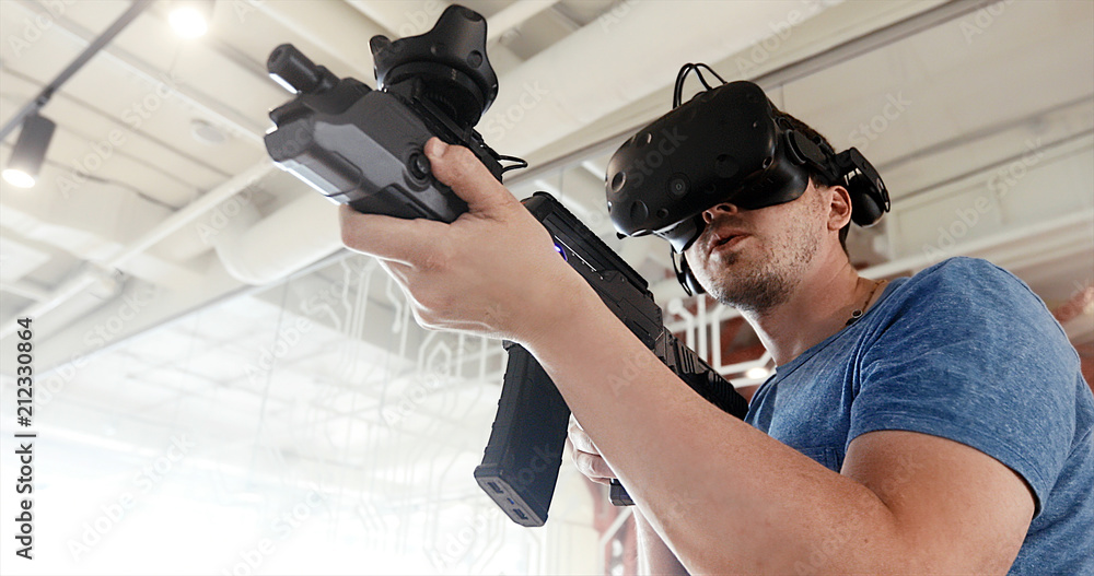 Guy playing VR sniper game with virtual reality gun and glasses