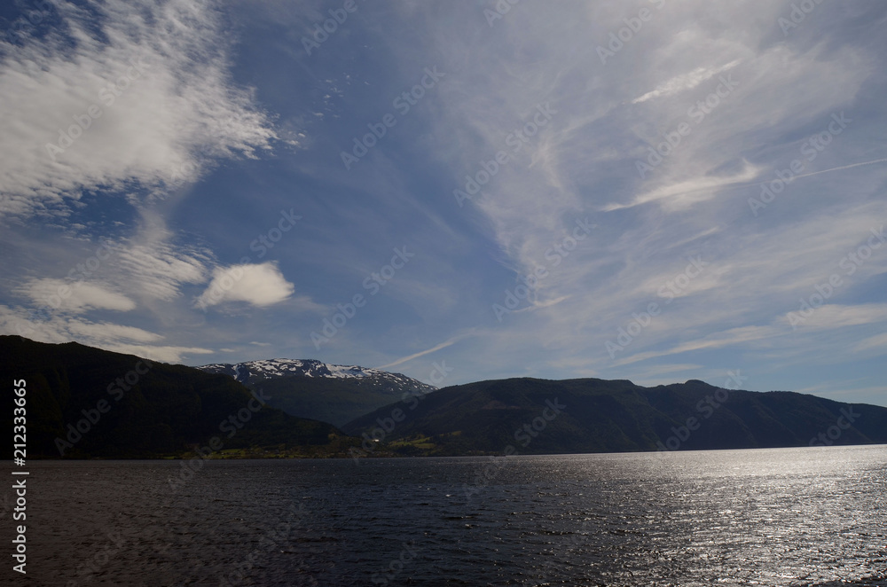 Mountains and fjord in Norway. Clouds and blue sky. Beautiful stunning views of mountains, water, sky, clouds and sun. Norwegian nature. Sognefjord
