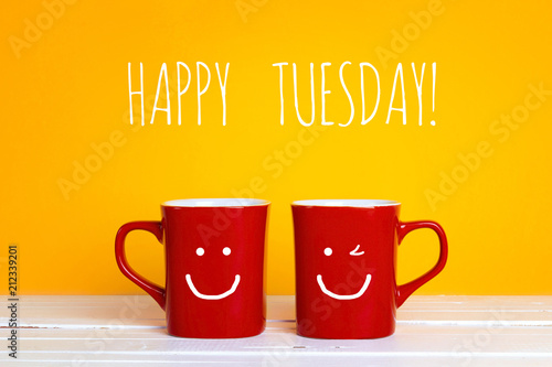 Two red coffee mugs with a smiling faces on a yellow background with copy space.