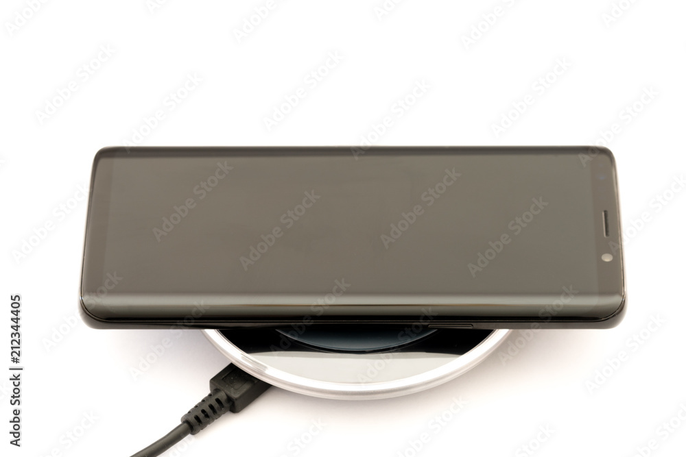 Modern black smartphone charging on wireless charger pad. Isolated on white background.