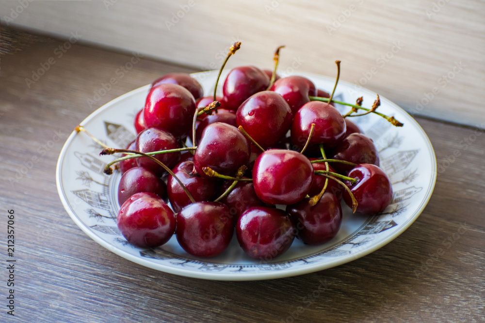 Fresh tasty cherry fruit on a plate on a wooden table. Beautiful juicy berries on a white plate. Fresh tasty cherry fruit on a plate on a wooden table. Beautiful juicy berries on a white plate.