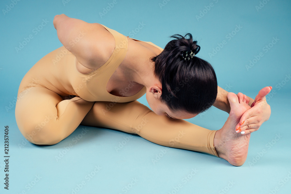 Obraz premium portrait of a beautiful and young yoga woman doing meditiret and relaxing in position on the floor on a blue background in the studio