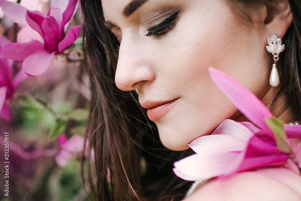 Portrait of young beautiful woman with long curly hair between pink magnolia tree, close up