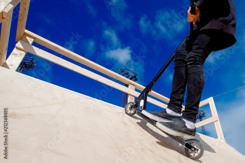 Man riding kick scooter in park ramp and springboards. Background Blue sky