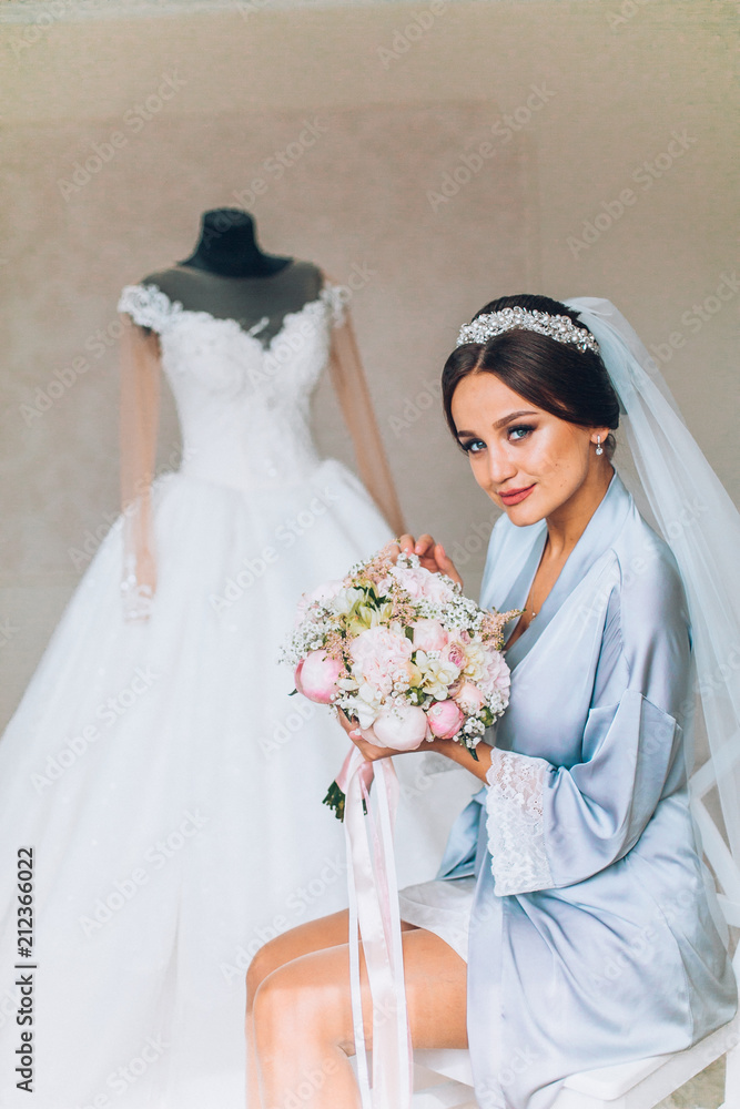 Naklejka premium Beautiful happy brunette bride in a stylish robe posing near manequin wedding dress, morning wedding preparation concept, bride portrait face closeup.