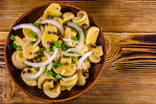 Ceramic plate with canned mushrooms on wooden table. Top view