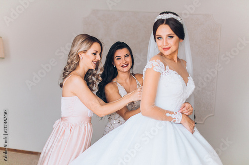 Obraz na płótnie Bride preparation before wedding ceremony. Pleasant young bridesmaids helping the bride to get ready w salonie
