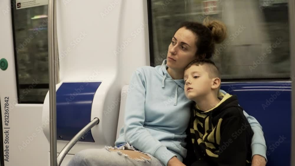 Mother and son traveling by subway train. Tired and sleepy boy lying on moms lap, woman stroking his head Mother and son traveling by subway train. Tired and sleepy boy lying on moms lap, woman stroking his head