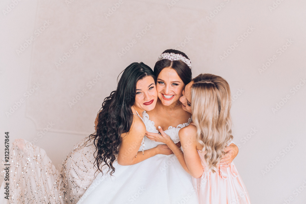 Happy bridesmaid hugging the bride in the bedroom in the morning. Before wedding ceremony. Bride preparing and wait groom. Happy bridesmaid hugging the bride in the bedroom in the morning. Before wedding ceremony. Bride preparing and wait groom.