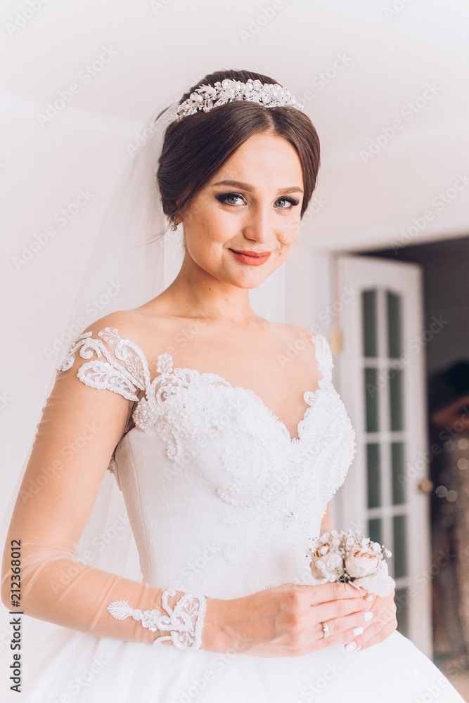 Attractive young bride before wedding ceremony holding the groom's buttonhole. flowers with pink roses, white carnation. Bride's Preparations. Wedding Morning. Attractive young bride before wedding ceremony holding the groom's buttonhole. flowers with pink roses, white carnation. Bride's Preparations. Wedding Morning.
