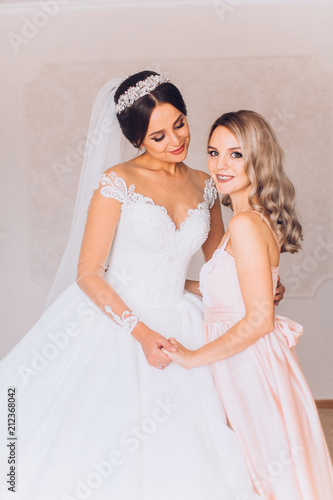 Happy gorgeous brunette bride in white dress having posingwith beautiful bridesmaid