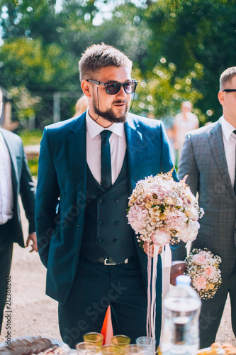 Groom and groomsmen have fun and walking to the restaurant. Wedding moment after ceremony. Guys in sunglasses and suite. Smiling wedding guests. photo
