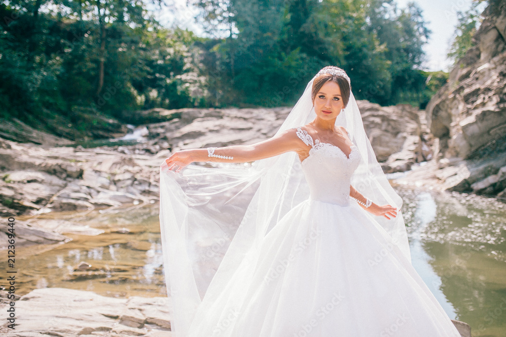 Beautiful bride walking on a fast river in the mountains. Wedding dress disperse of wind. Beauty portrait of a bride around amazing nature. Beautiful bride walking on a fast river in the mountains. Wedding dress disperse of wind. Beauty portrait of a bride around amazing nature.