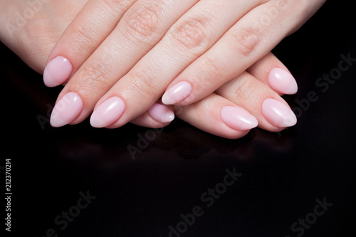 Women s hands with perfect Nude manicure. Nail Polish is a natural pale pink shade. Black background