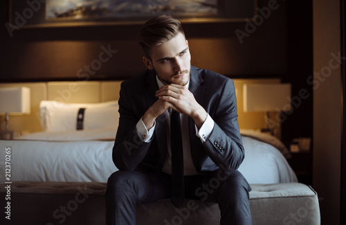 Young handsome man relaxing at his apartment in a hotel after business meeting. Business trip. Booking hotel during your vacation. Businessman in luxury room of the expensive beautiful hotel. 