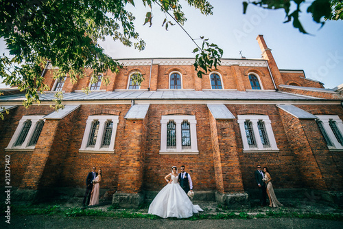 Happy fun newlyweds posing in street with bridesmaids and groomsmen. Bride and groom with friends near old church. photo