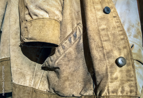 Old jacket of canvas.Special protective clothing of the welder from natural linen cloth hangs on the wall. He has scuffing damage, contamination and repair marks.
