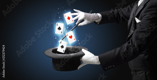 Magician with white gloves conjuring playing cards from a cylinder with magic wand photo