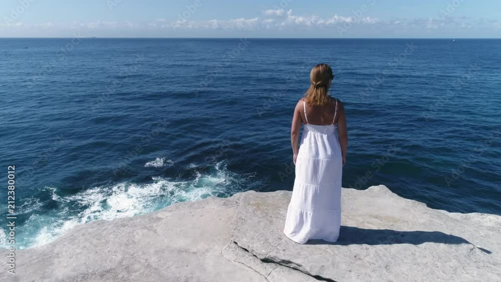 Beautiful woman stands on a cliff edge over the ocean. Dolly shot Beautiful woman stands on a cliff edge over the ocean. Dolly shot