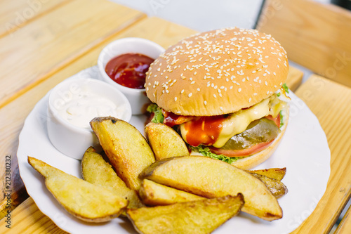 Homemade cheese burger or hamburger on wood plate served with french fries put on black granite table with copy space. Fast food for breakfast or lunch.