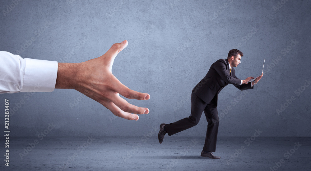 Young miniature businessman running from a big hand with blueish grey background Young miniature businessman running from a big hand with blueish grey background