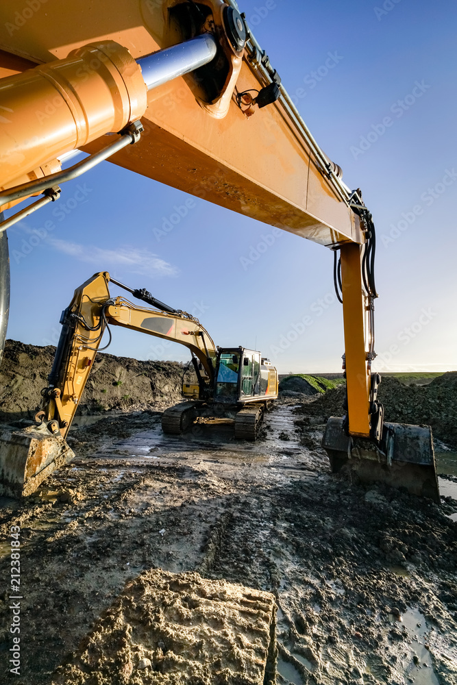 Fototapeta premium Zwei Bagger auf einer schlammigen Baustelle, Hochformat