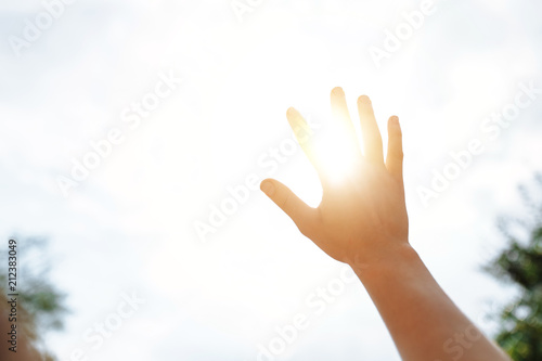 a hand reaches for the sky and covers the sun, the sun's rays make their way through the hand, close - up, bright sunlight