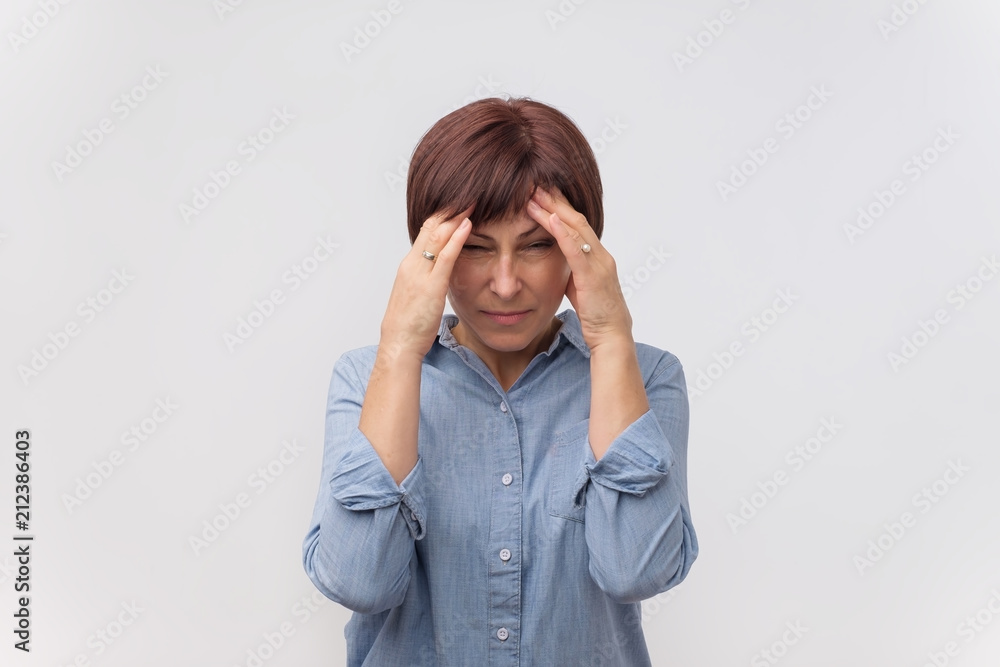 Portrait of worried mature woman touching her temples feeling stress, on gray background Portrait of worried mature woman touching her temples feeling stress, on gray background
