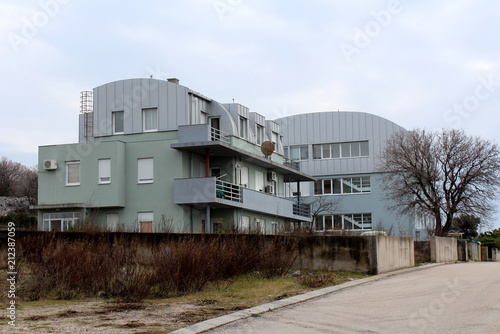 Small apartment building with curved metal roof surrounded with concrete wall and small dried winter vegetation