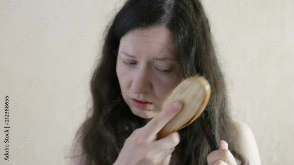 Long-haired dark blond woman combs her hair and has a frustrated face Close-up, indoors, real time Long-haired dark blond woman combs her hair and has a frustrated face Close-up, indoors, real time