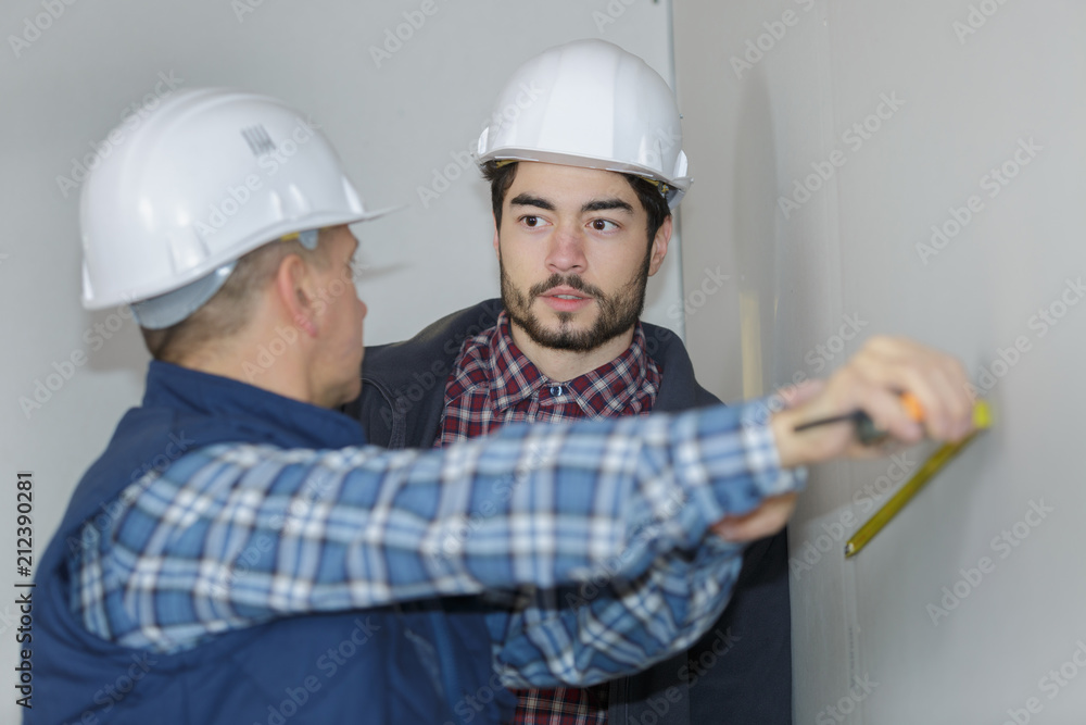 two workmen measuring interior wall with tae measure two workmen measuring interior wall with tae measure