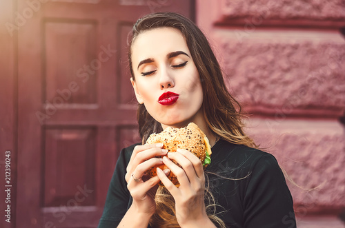 the girl chews a hamburger with pleasure. high-calorie but tasty food
