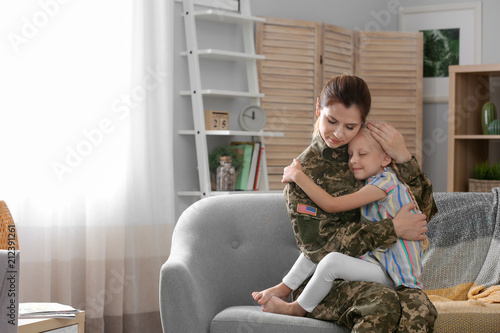 Woman in military uniform with her little daughter on sofa at home photo